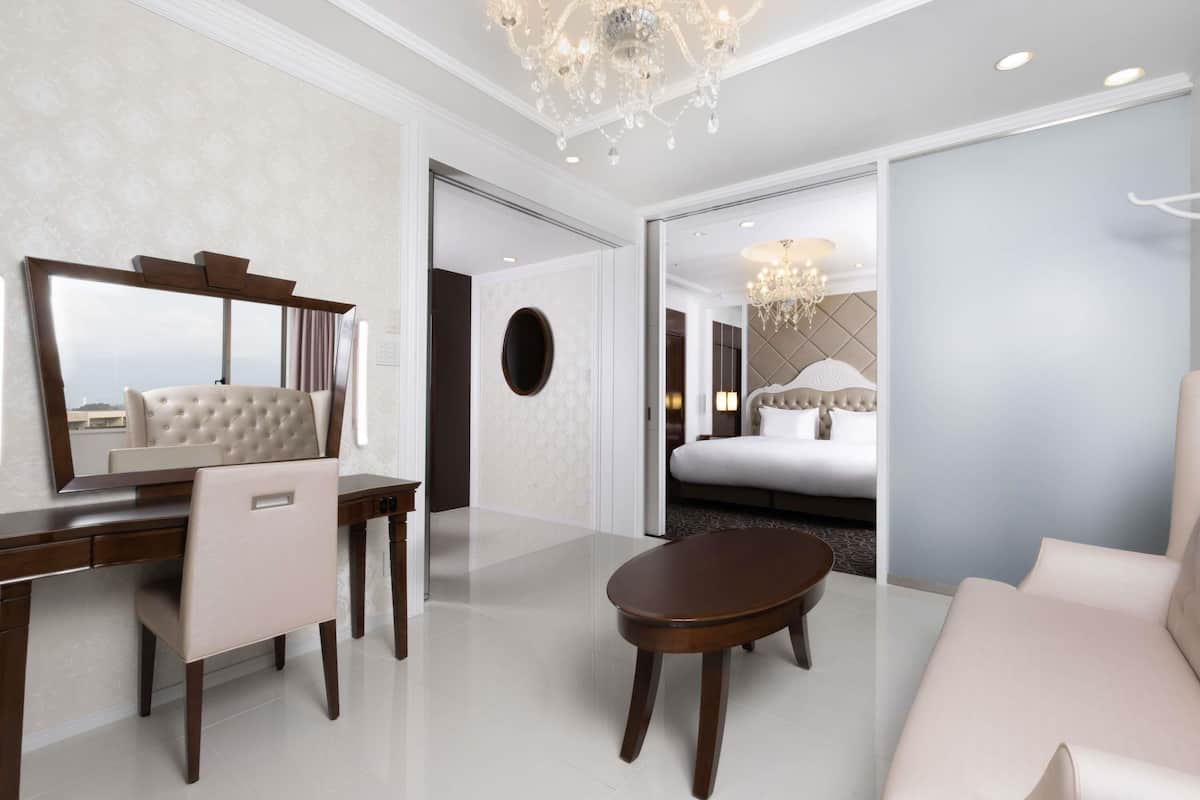 Ein modernes Hotelzimmer mit einem großen Bett, einer Sitzecke mit Sofa und Sessel, einem Schreibtisch mit Stuhl und einer Chandelier.