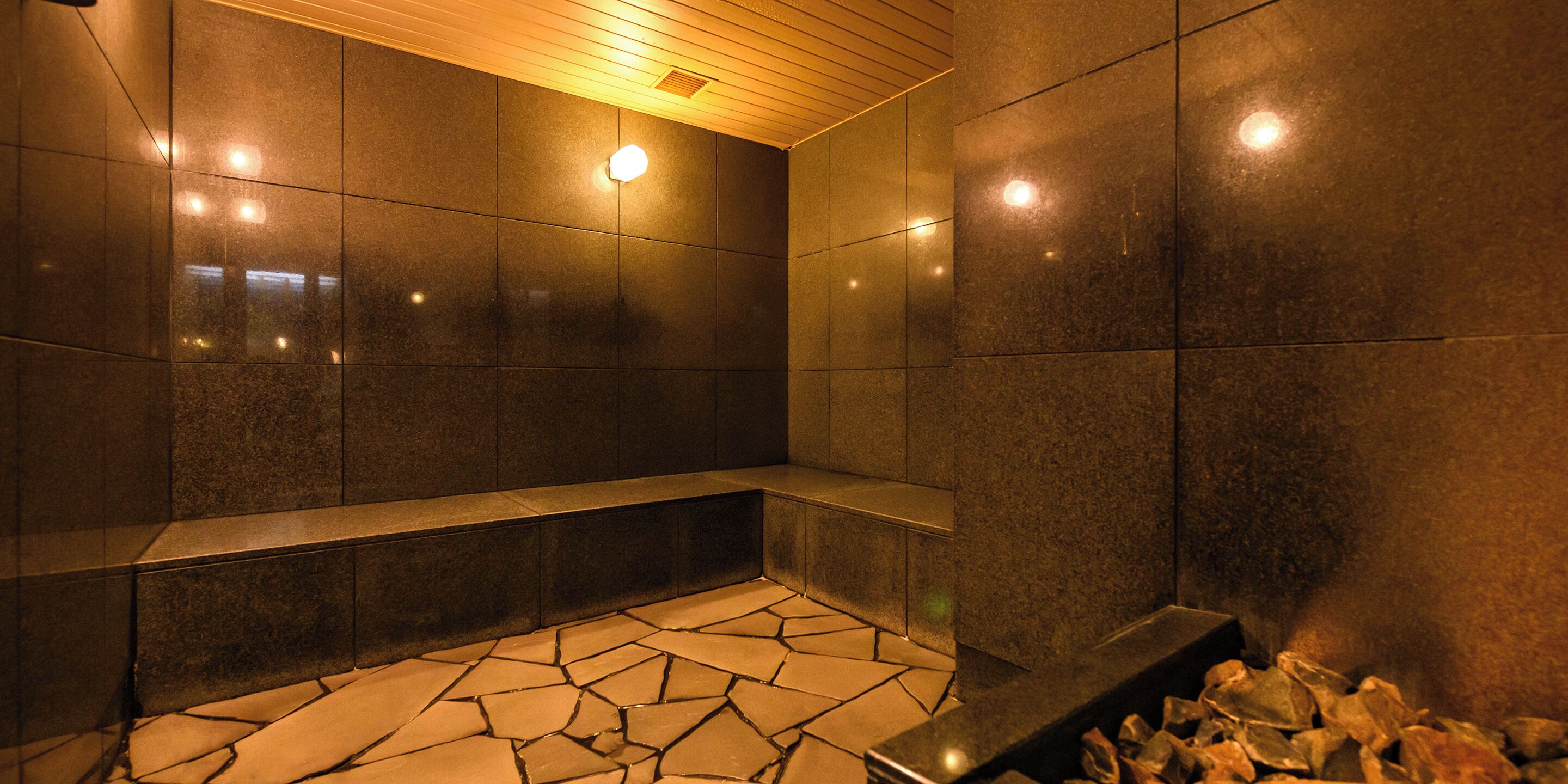A modern bathroom with dark tiled walls, a stone-patterned floor, and a bench.