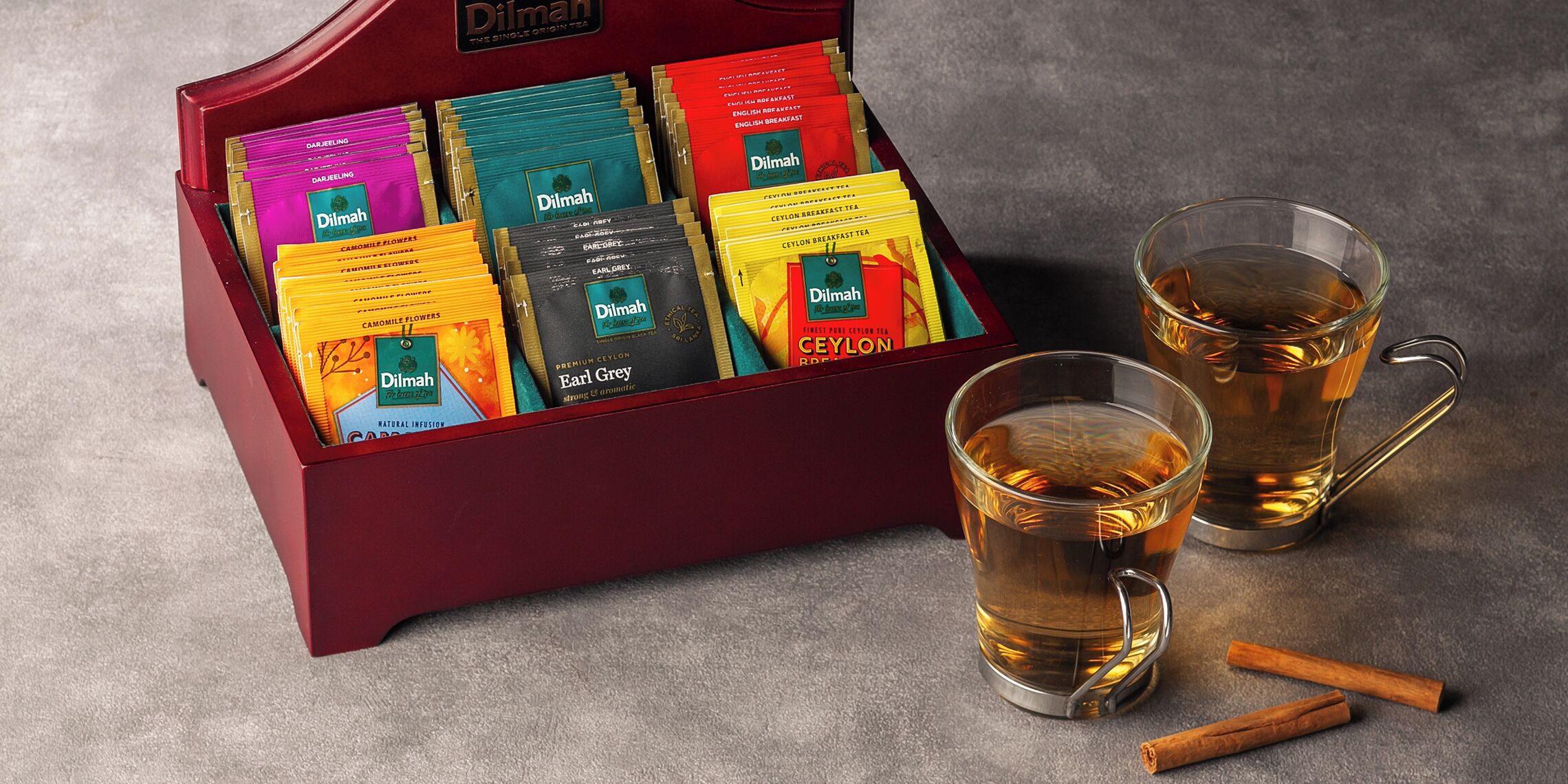 Une boîte de sachets de thé et deux verres de thé avec des bâtons de cannelle.