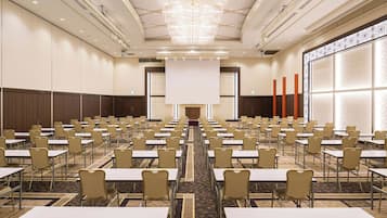 A conference room with rows of tables and chairs, a large screen at the front, and a patterned wall on one side.