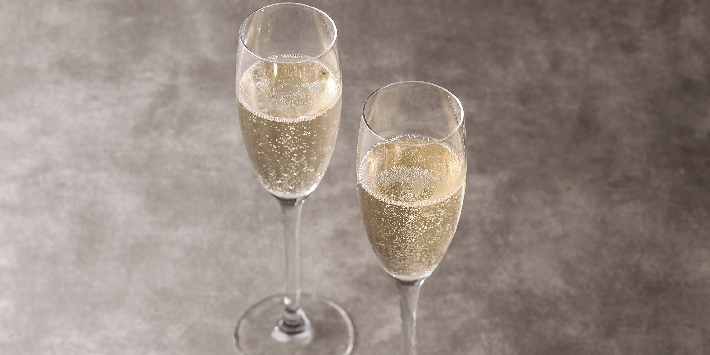 Two champagne flutes filled with a bubbly beverage, placed on a textured surface.