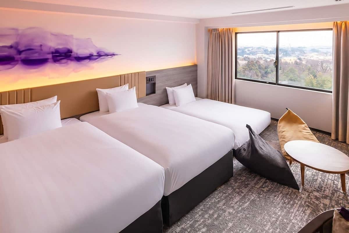 Ein Hotelzimmer mit drei Betten, einem kleinen Tisch, einem Stuhl und einem großen Fenster mit Blick.
