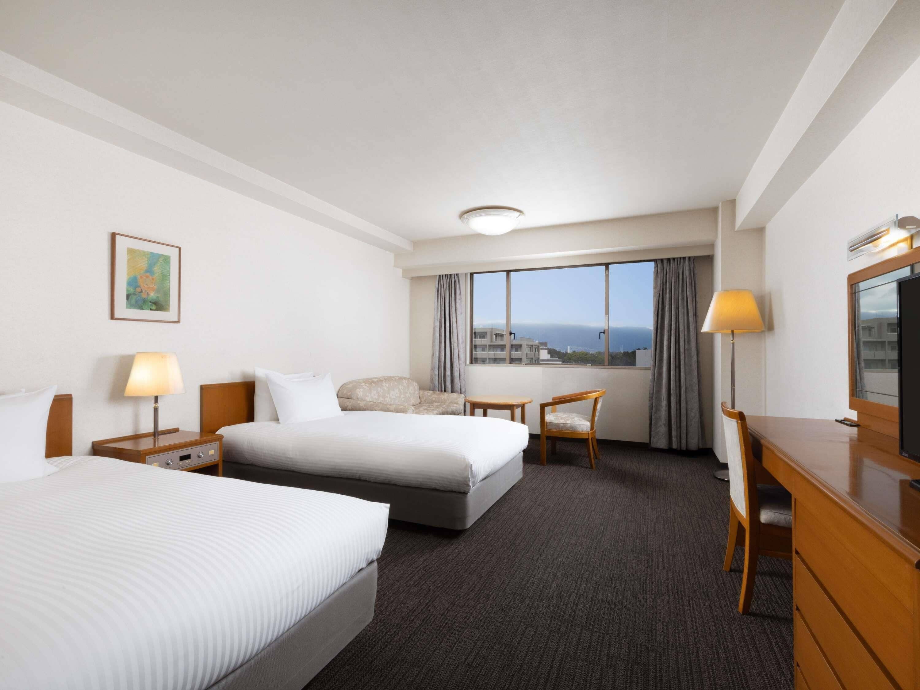 A hotel room with a bed, a desk, a chair, a TV, and a window with a view.