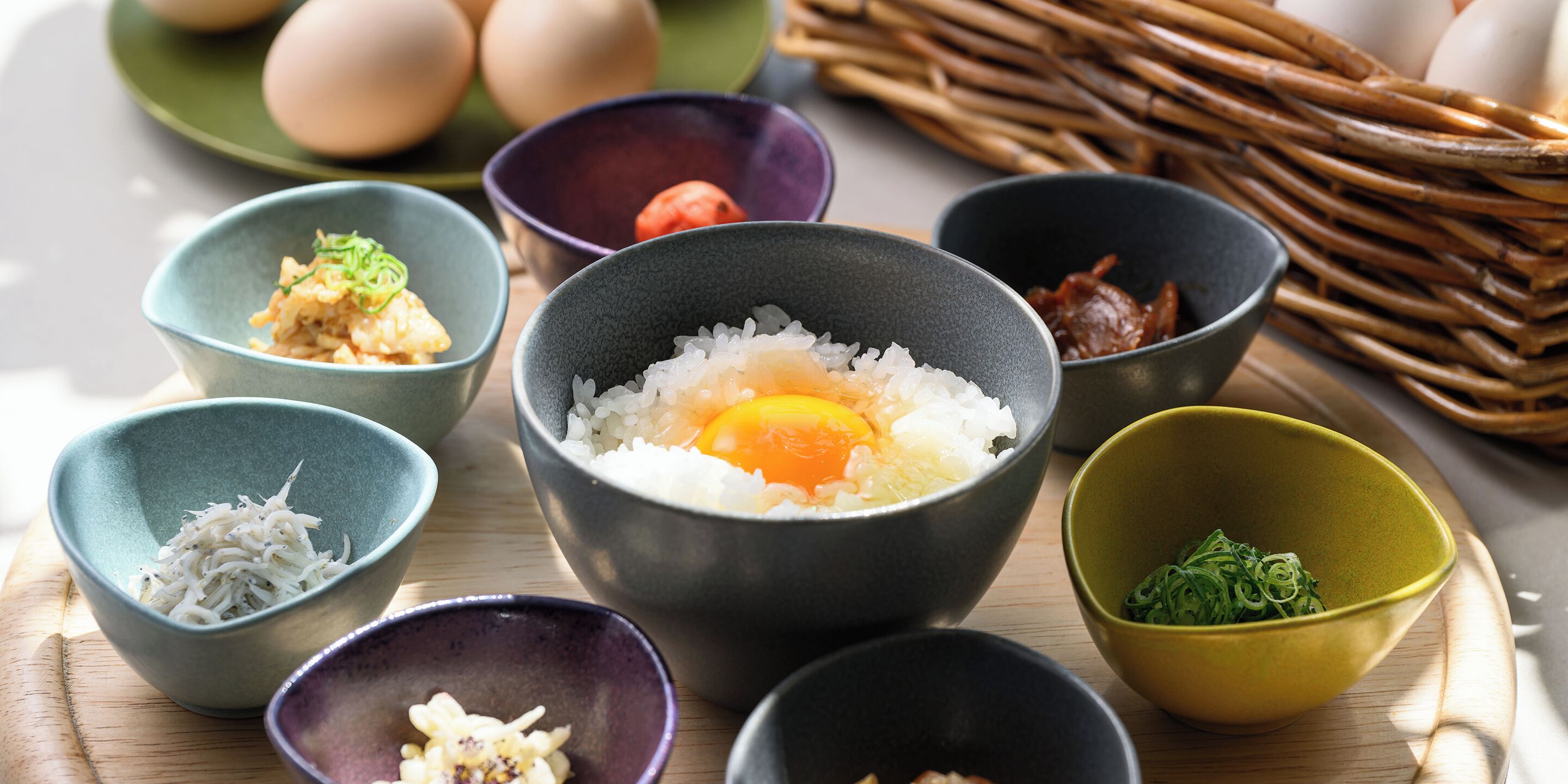 A variety of bowls containing different food items, including rice, eggs, and vegetables, arranged on a wooden surface.