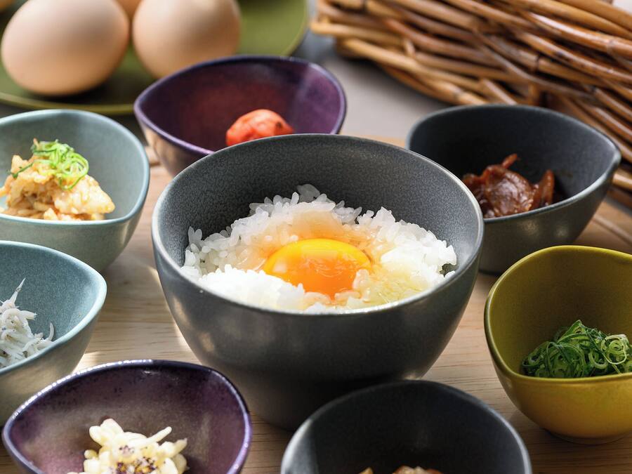 A variety of bowls containing different food items, including rice, eggs, and vegetables, arranged on a wooden surface.