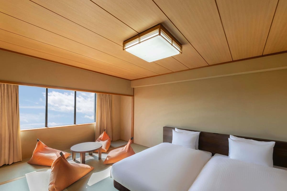 Ein Hotelzimmer mit einem großen Bett, zwei Kissen, einem runden Tisch mit Stühlen und Blick auf den Himmel durch das Fenster.