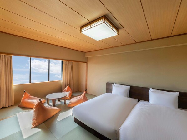 Habitación de hotel con una cama grande, dos almohadas, una mesa redonda con sillas y vistas al cielo a través de la ventana.