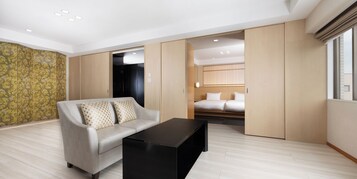 Una habitación de hotel moderna con un sofá, una mesa de centro negra, una cama con ropa de cama blanca y un armario con puerta corredera.