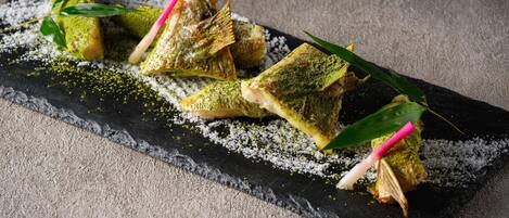 A dish with green and white powdered toppings, garnished with green leaves and pink sticks, on a black slate plate.