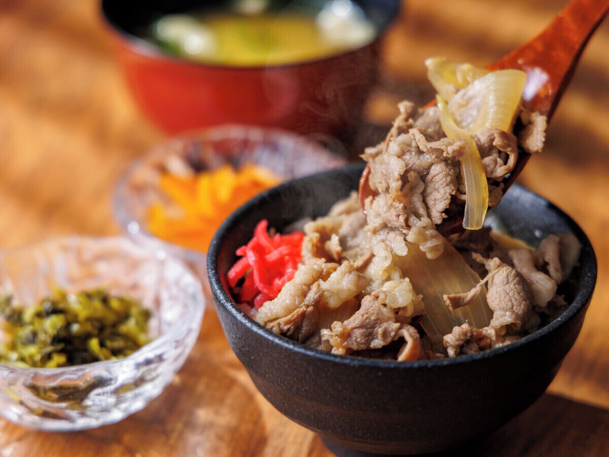 A bowl of food with a spoon lifting a piece of meat and vegetables.