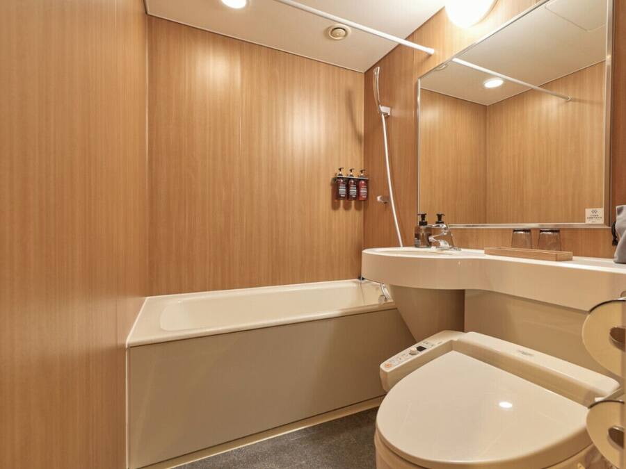 A modern bathroom with a wooden wall, a bathtub, a toilet, and a sink with a mirror.