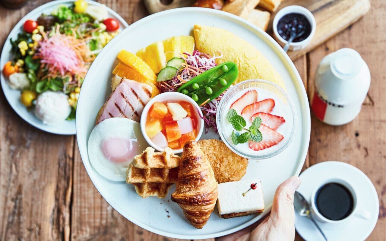 A breakfast plate with various foods including waffles, a croissant, and a salad.
