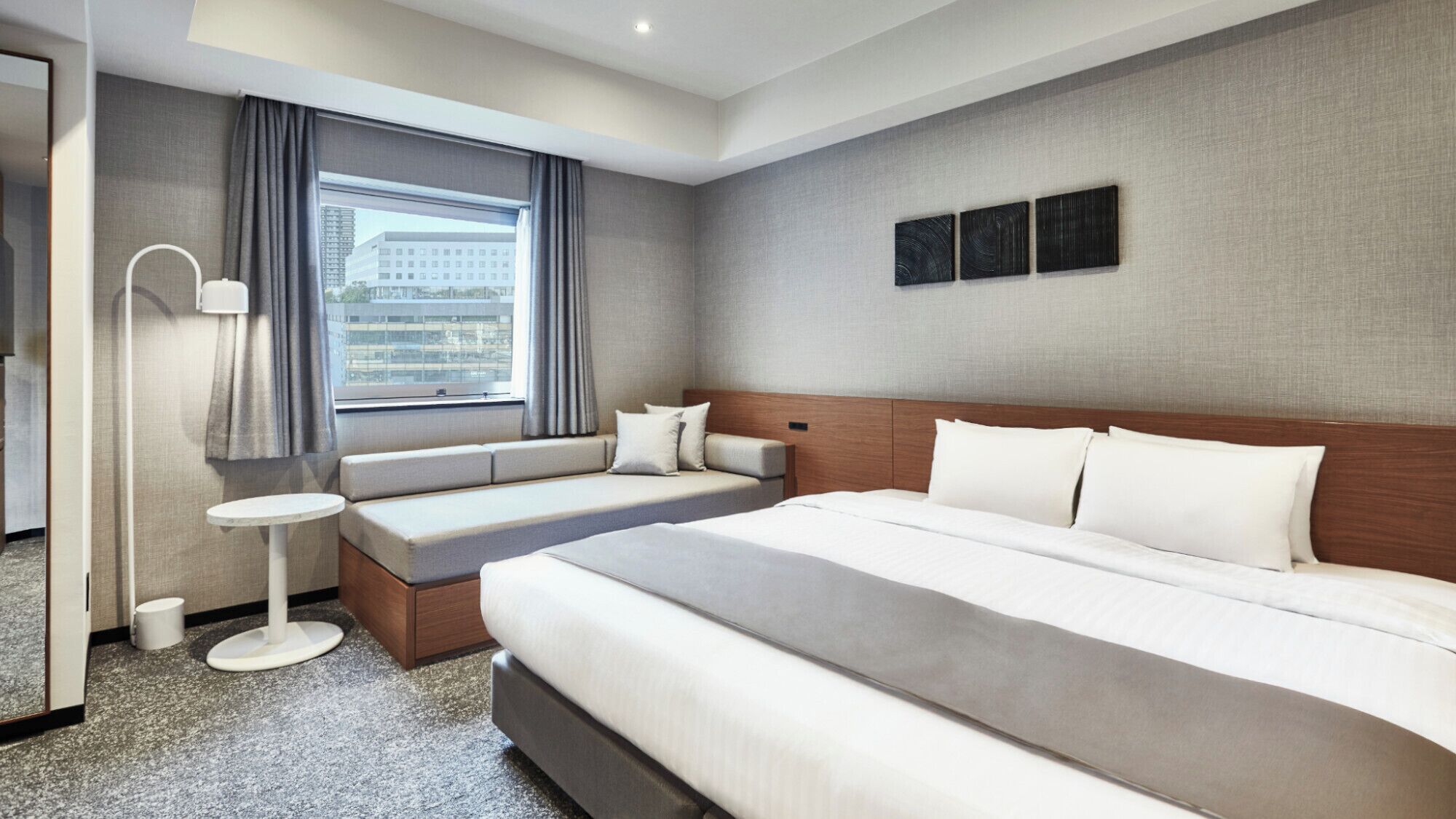 A hotel room with a large bed, a seating area, a bedside table, and a window with curtains.