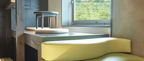 A modern kitchen with a built-in stove, a window with a view of greenery, and a yellow cushioned bench.