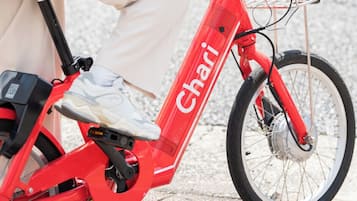 A red electric bike with the brand name 'Chari' on the frame, a basket on the front, and a kickstand.