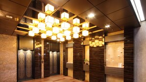 An elevator area with a modern design, featuring a patterned wall and a reception desk with a plant. - Takamatsu Tokyu REI Hotel (Takamatsu)