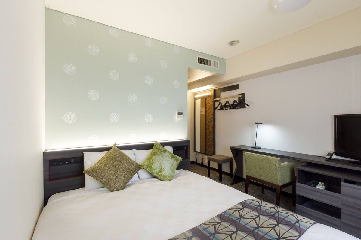 A hotel room with a bed, a desk, a television, and a mirror.