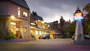 A motel with a neon sign, a car parked in front, and a well-lit entrance. - Pacific Park (Dunedin)