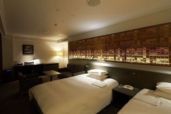 Une chambre d’hôtel avec un grand lit, un bureau avec une chaise, une petite table, une lampe et un mur orné d’un motif décoratif.
