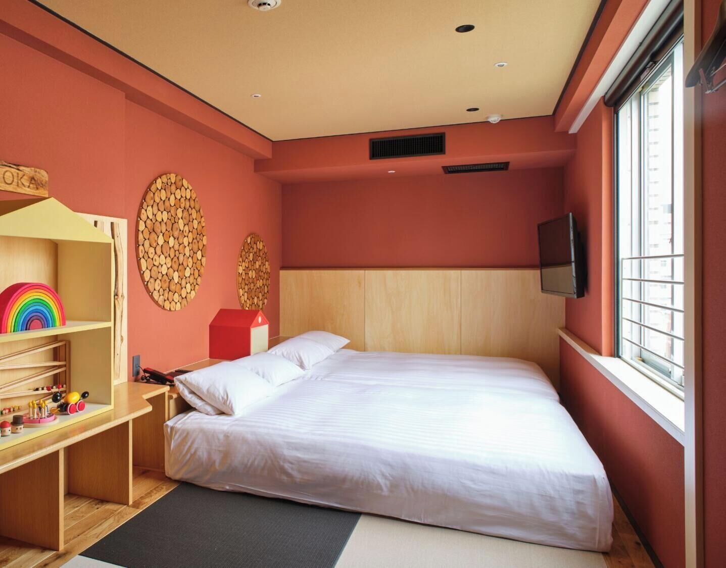A bedroom with a bed, a TV, a window, a wooden headboard, and a shelf with toys.