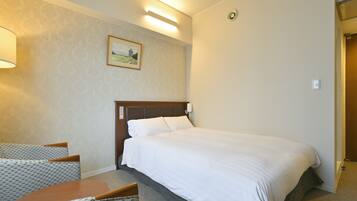 A hotel room with a bed, a desk, and a chair. There is a painting on the wall and a light fixture above the bed.