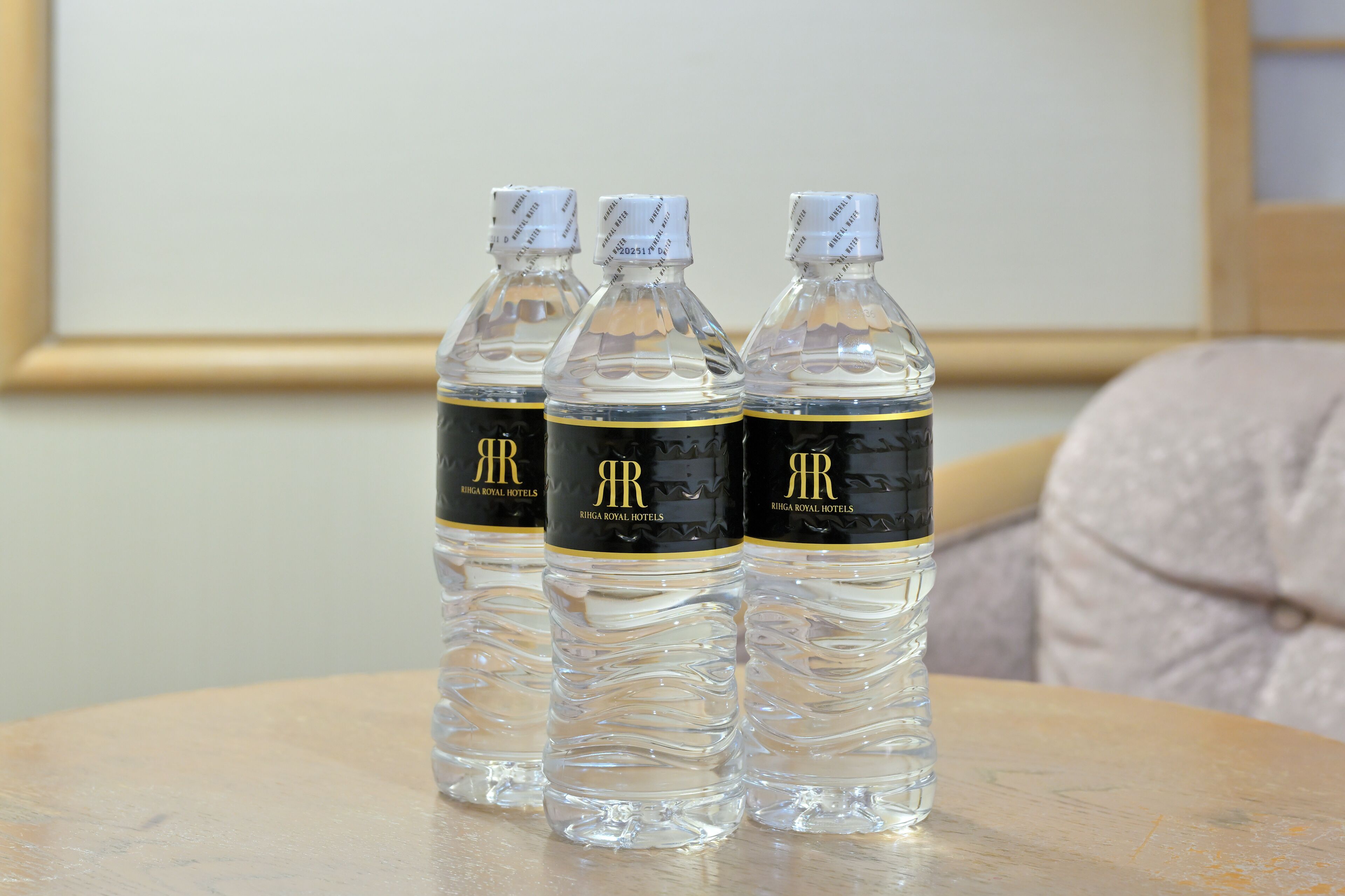 Tres botellas de agua transparente con etiquetas doradas y negras sobre una mesa redonda.