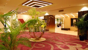 A lobby with a red carpet, a central glass table with plants, and a staircase in the background. - Rihga Hotel Zest Takamatsu (Takamatsu)