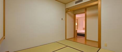 A room with tatami mats, a wooden door, and a bed in the adjacent room.