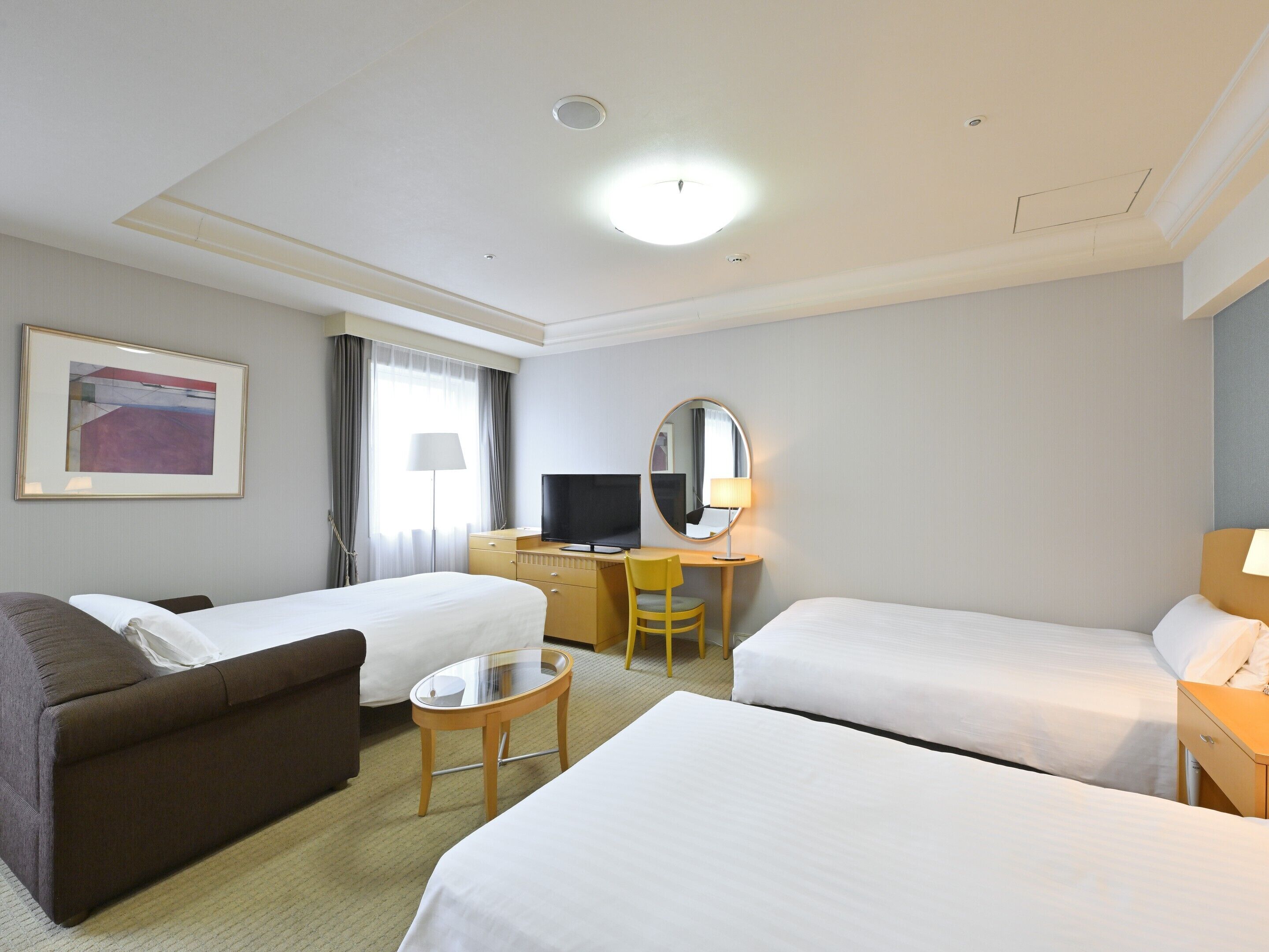 Habitación de hotel con dos camas individuales, un sofá, un escritorio con televisor, un espejo y un cuadro en la pared.