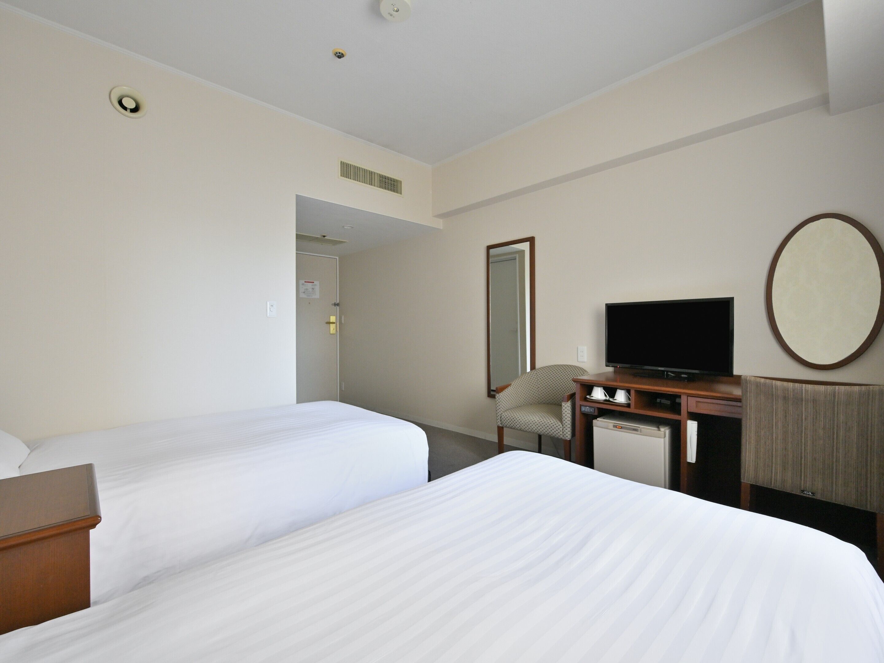 A hotel room with two beds, a desk with a television, a chair, and a large mirror on the wall.