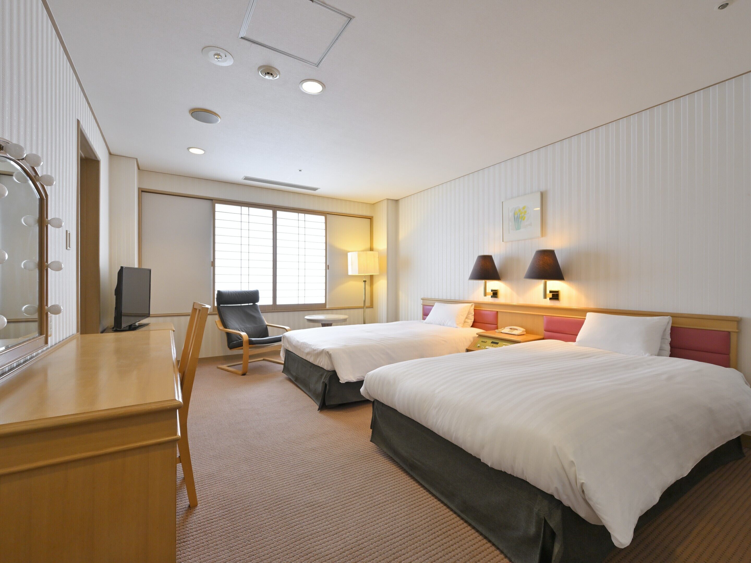 Een hotelkamer met twee bedden, een bureau met spiegel, een stoel, een televisie en een raam.