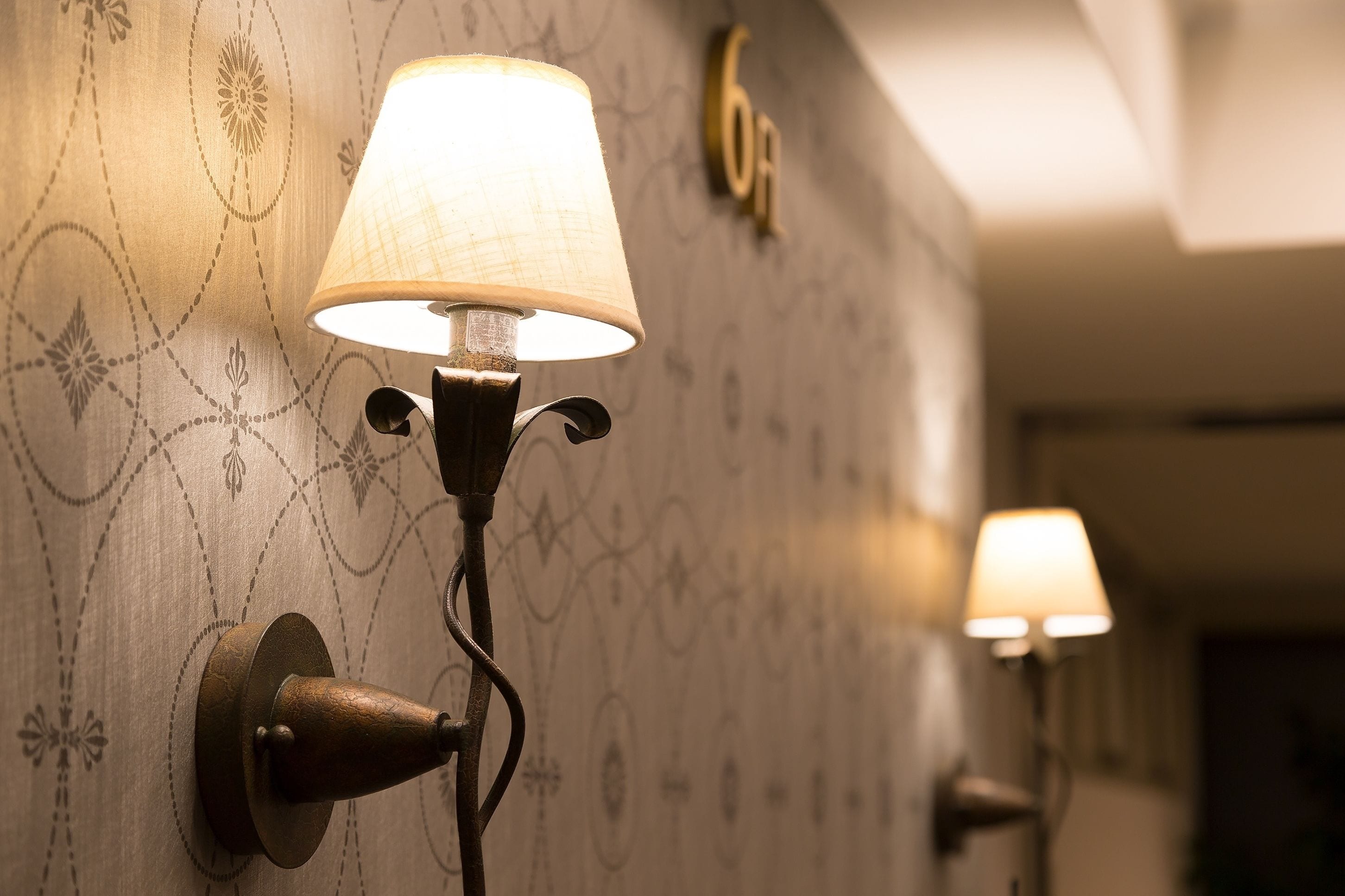 Wall-mounted sconces with a patterned wallpaper background and a number "6" sign.
