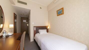 A hotel room with a single bed, a wooden desk with a chair, a mirror, and a wall-mounted light fixture.
