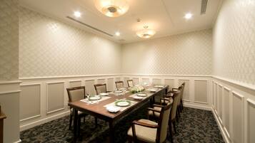 A conference room with a long table set for a meeting, surrounded by chairs, with patterned wallpaper and recessed lighting.