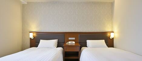 A hotel room with two single beds, a bedside table with a phone, and a wall-mounted light fixture.