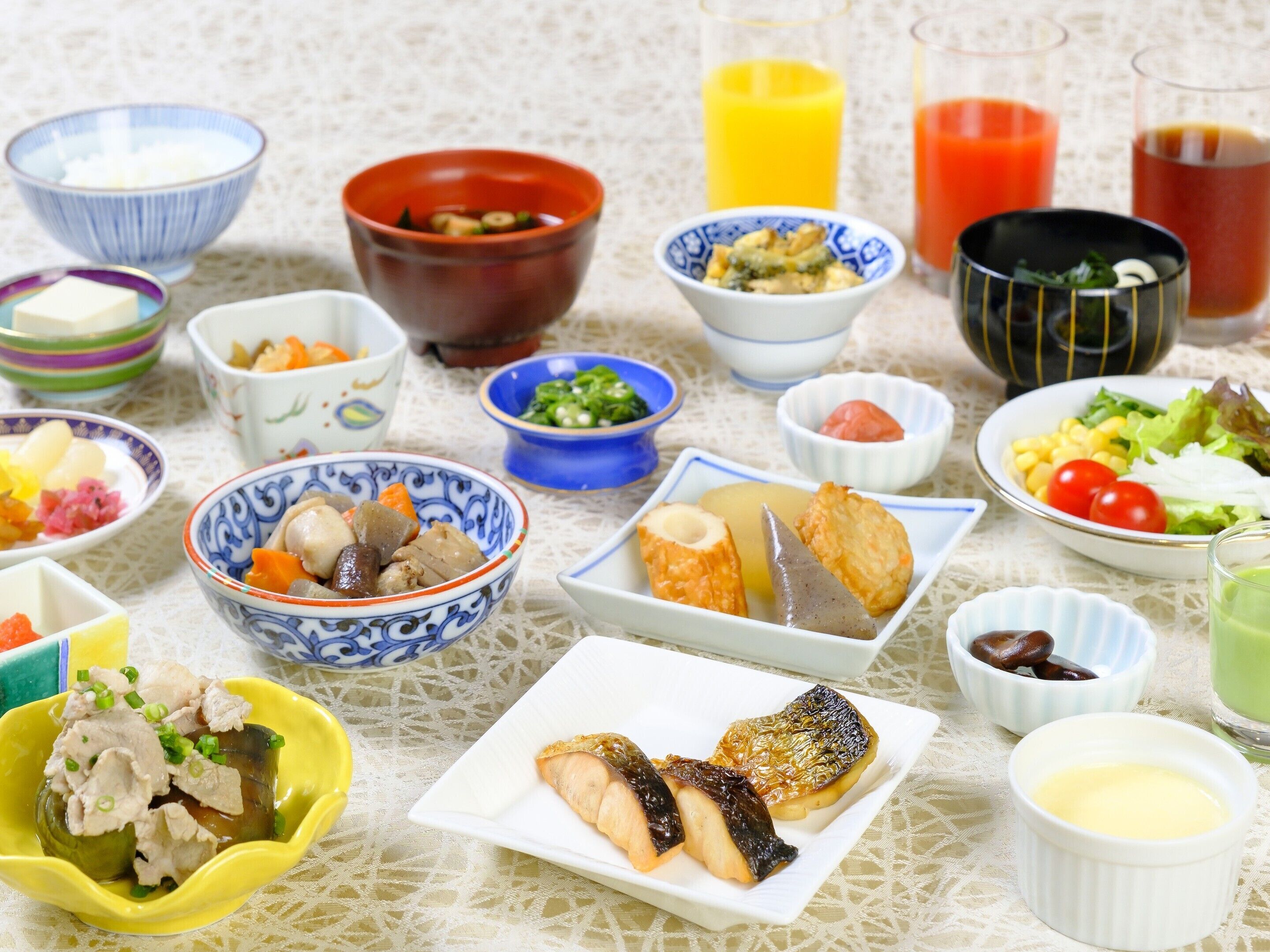 Variedad de platos y bebidas sobre una mesa, incluyendo cuencos de comida, un plato de pescado y vasos de jugo.