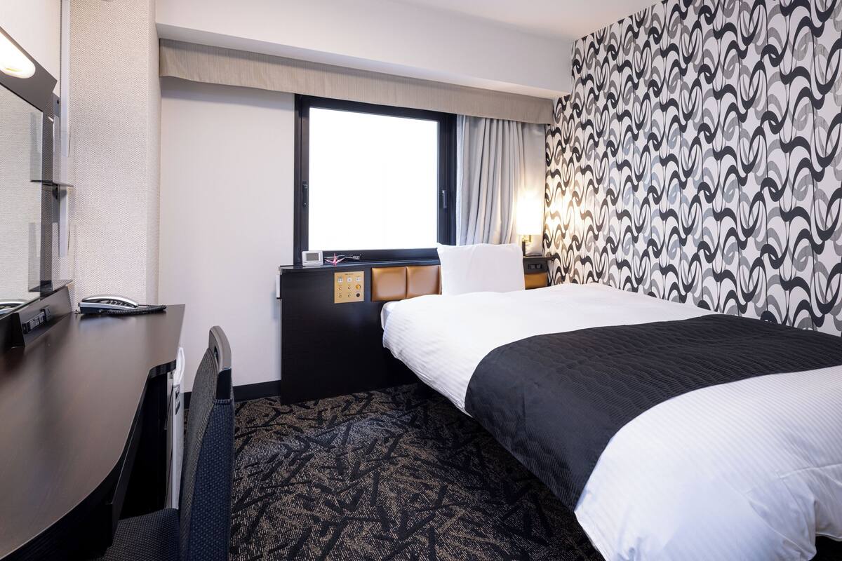 A hotel room with a bed, a desk, a telephone, and a window.