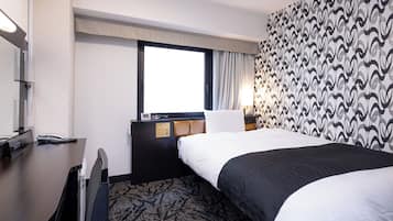 A hotel room with a bed, a desk, a telephone, and a window.