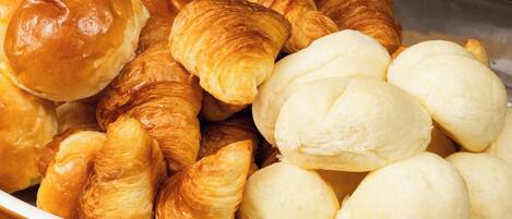 A variety of baked goods including croissants and rolls in a glass display case.
