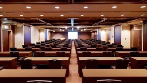 Ein Konferenzraum mit Tischen und Stühlen, einem Rednerpult vorne und Türen an den Seiten.