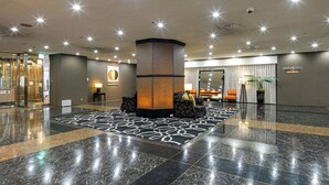 Eine geräumige Lobby mit einer zentralen Säule, einem gemusterten Teppich und einem Empfangsbereich mit Sitzgelegenheiten.