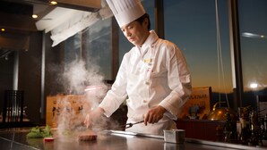 Un chef con uniforme blanco y gorro alto, preparando comida con vapor saliendo de la sartén.