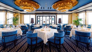Un comedor con mesas redondas, sillas tapizadas en azul y una alfombra estampada.