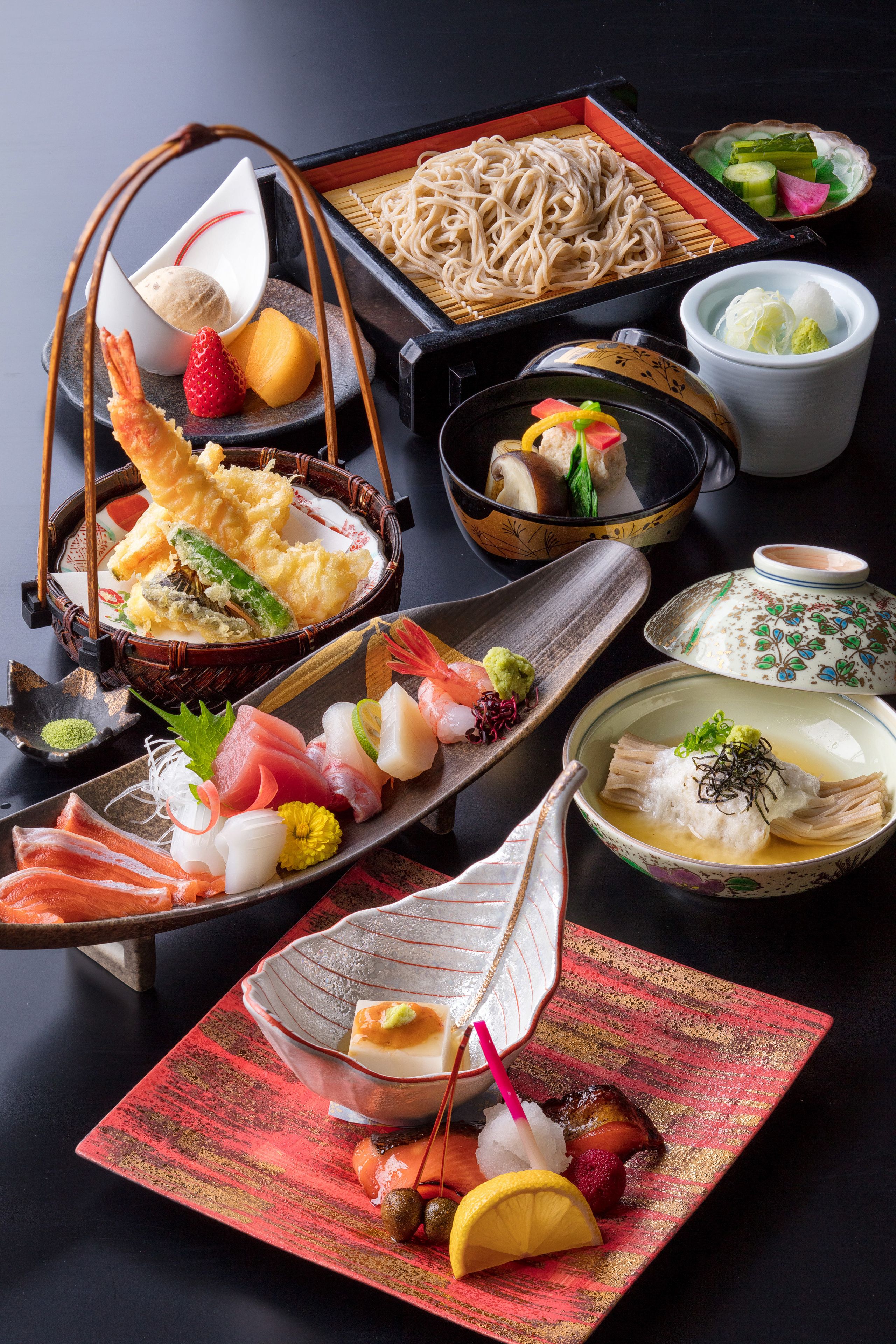 A variety of Japanese dishes including sushi, sashimi, and noodles, arranged on a table.