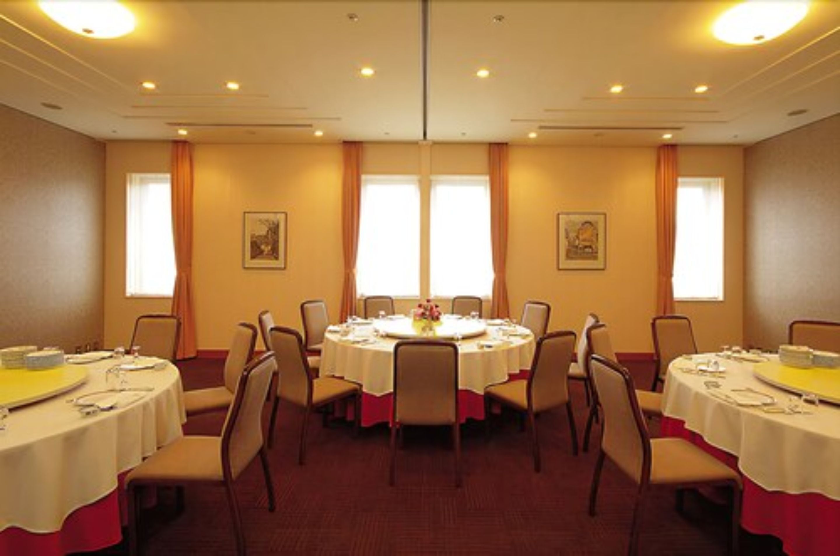 Un salón de conferencias con mesas redondas, sillas y grandes ventanales con cortinas.