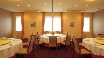 Un salón de conferencias con mesas redondas, sillas y grandes ventanales con cortinas.
