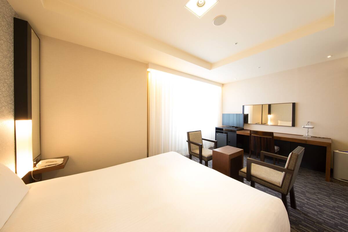 Una habitación de hotel con una cama grande, un escritorio con silla, un televisor y un espejo.