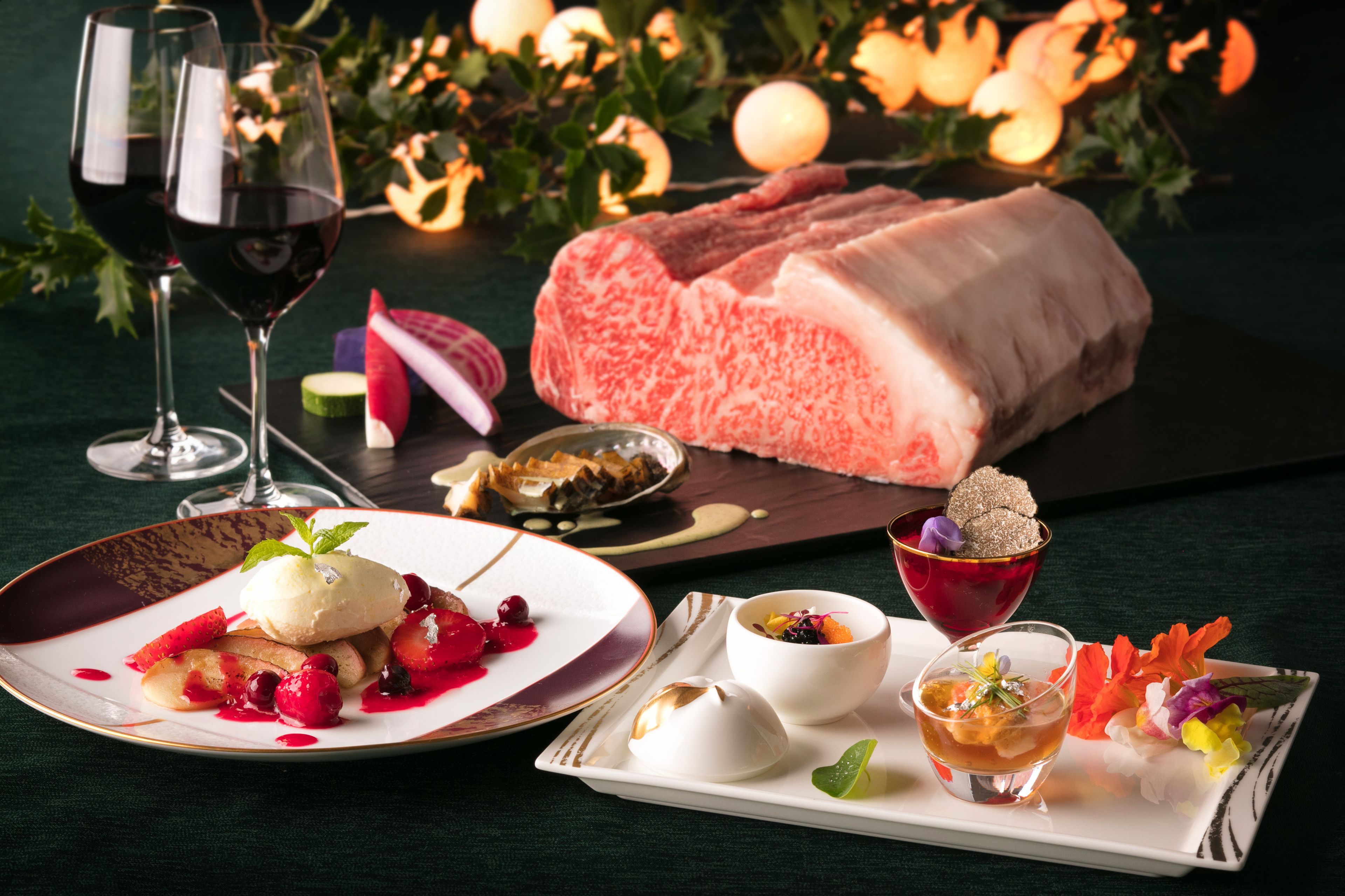 A dining table with a large piece of meat, a plate of fruit, and a glass of red wine.