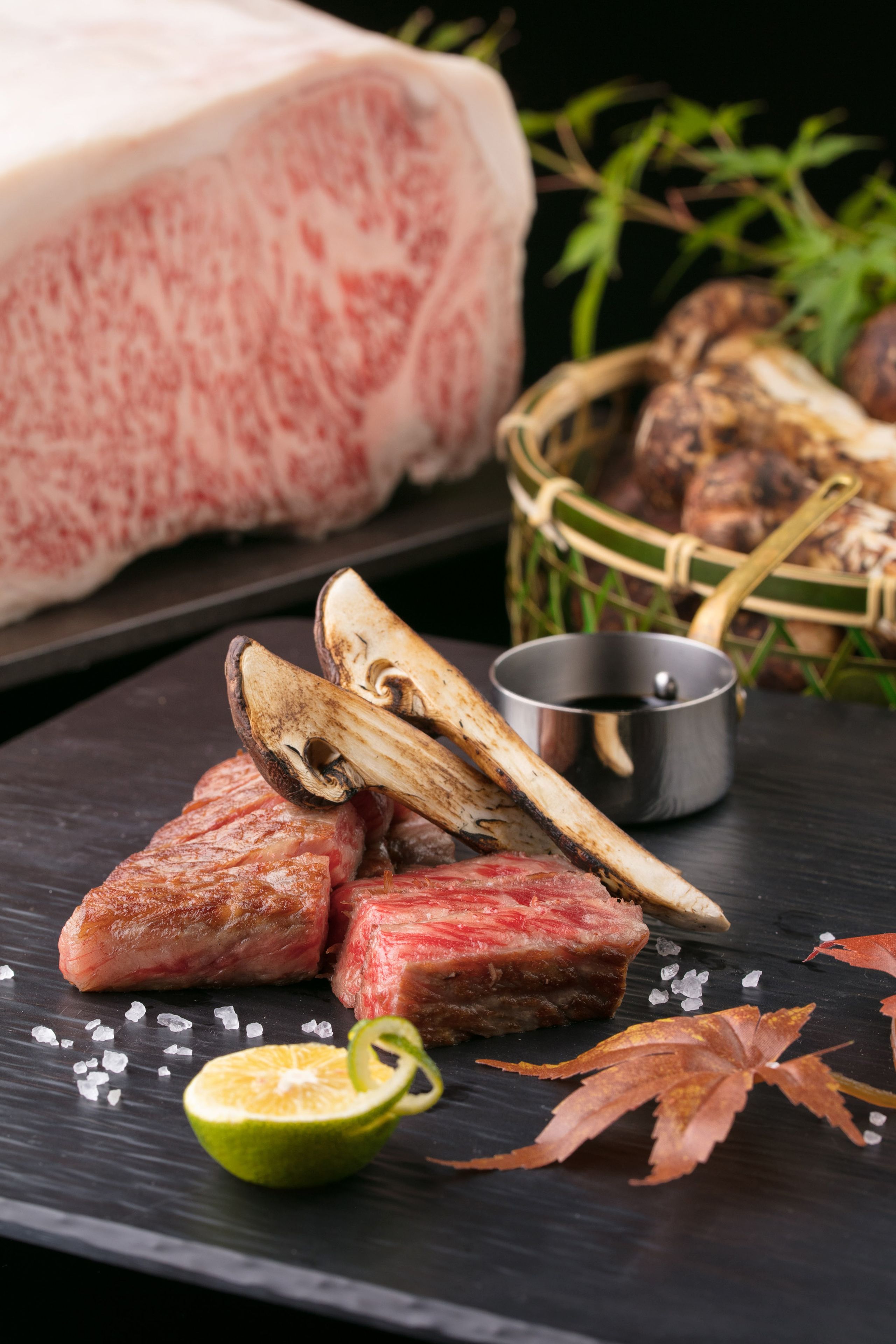 Assortimento di carni e funghi su una superficie scura in ardesia, con spicchio di lime e sale.