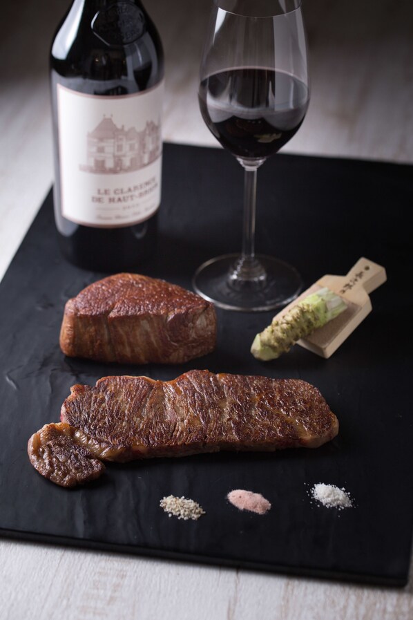 Um bife, uma garrafa de vinho e uma taça de vinho sobre um bloco de ardósia preta.
